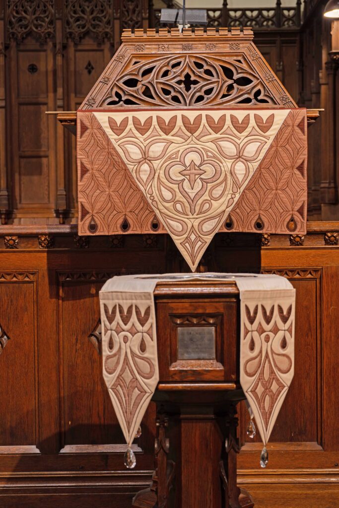 These complementary pieces were commissioned by Ann MacIsaac (1933-2016) in memory of her husband of 43 years Robert Forbes, both longtime members of First Church. The colors and designs of these pieces were inspired by the reredos and carvings at the end of the pews. The glass crystals at the ends of the font pieces are from a chandelier and represent drops of water.